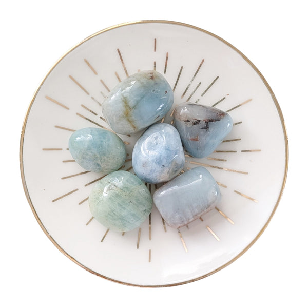 Aquamarine crystal tumblestones displayed on a small gold rimmed dish. 