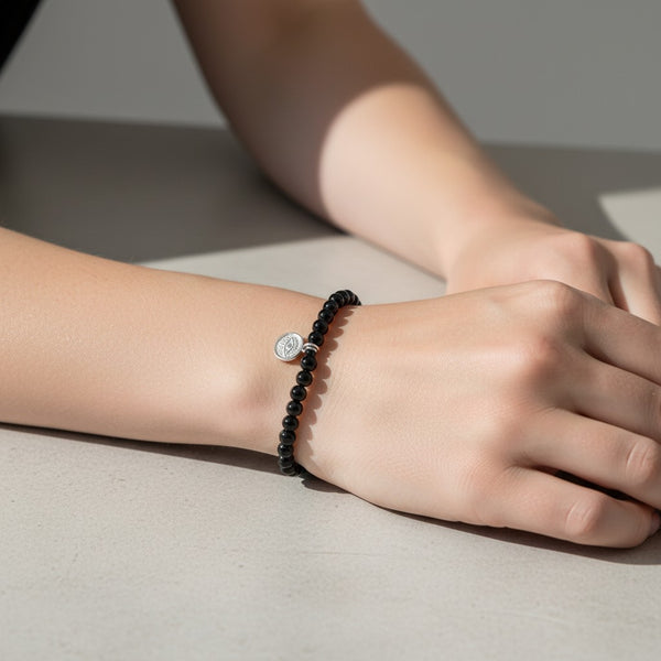 Black agate beaded crystal bracelet on a wrist with a small 925 Sterling Silver Evil Eye charm hanging. 