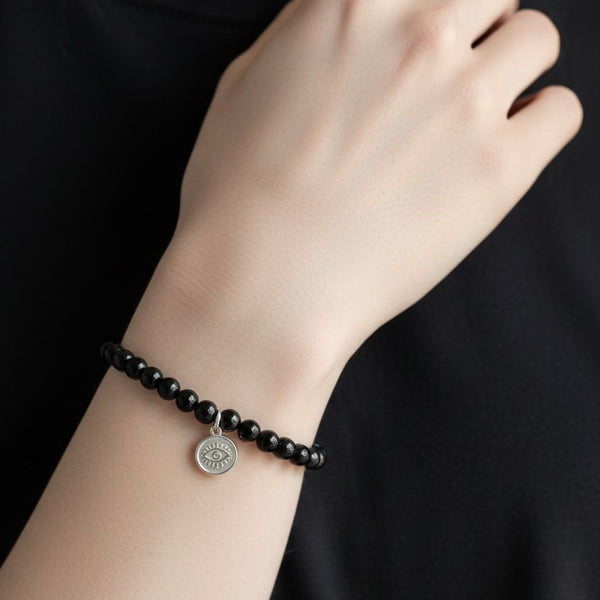Black agate beaded crystal bracelet on a wrist with a small 925 Sterling Silver Evil Eye charm hanging. 